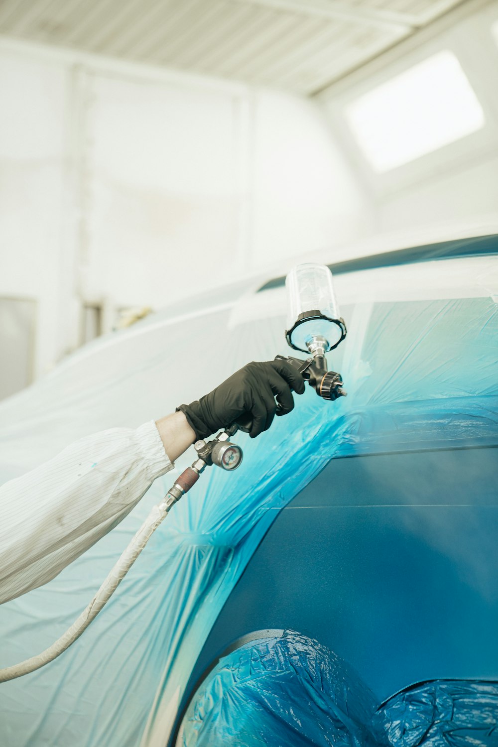 A gloved hand spraying basecoat onto a panel